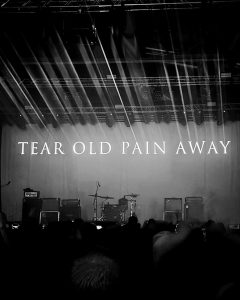 Schwarz/Weiß Foto auf dem Konzert von Amenra in Bochum mit dem Schriftzug "Tear Old Pain Away"